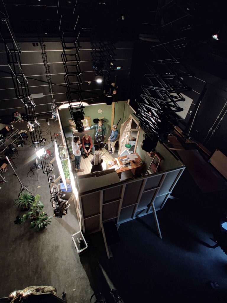 Elokuvastudioon lavastettu huone, jossa kuvausryhmä työskentelee kuvattuna ylhäältä. 